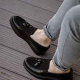 Black patent leather loafer showing front detail and tassel, with jeans
