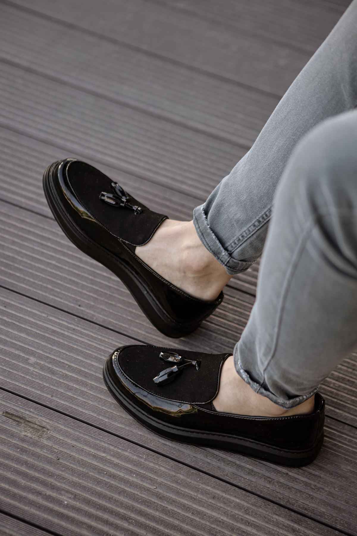 Black patent leather loafer showing front detail and tassel, with jeans