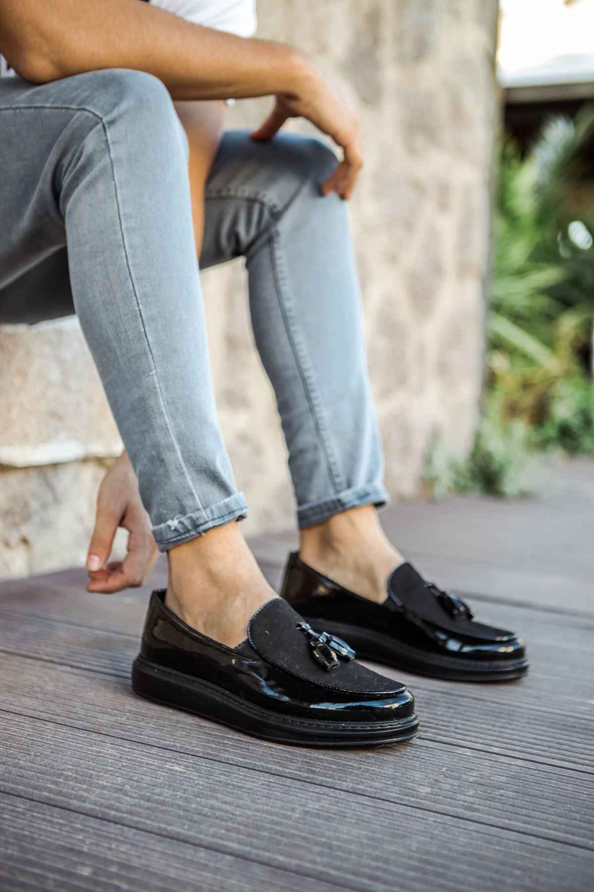 Black patent leather loafers with tassel detail, worn with light blue jeans