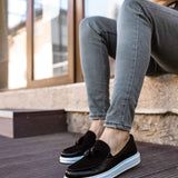 Black tassel loafers with white sole, worn with blue jeans
