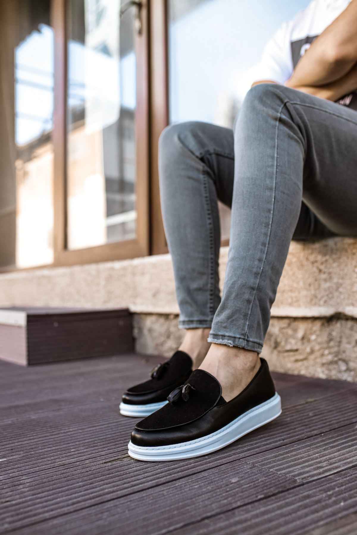 Black tassel loafers with white sole, worn with blue jeans