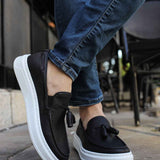 Men's black loafers with tassel strap and white midsole, worn with jeans