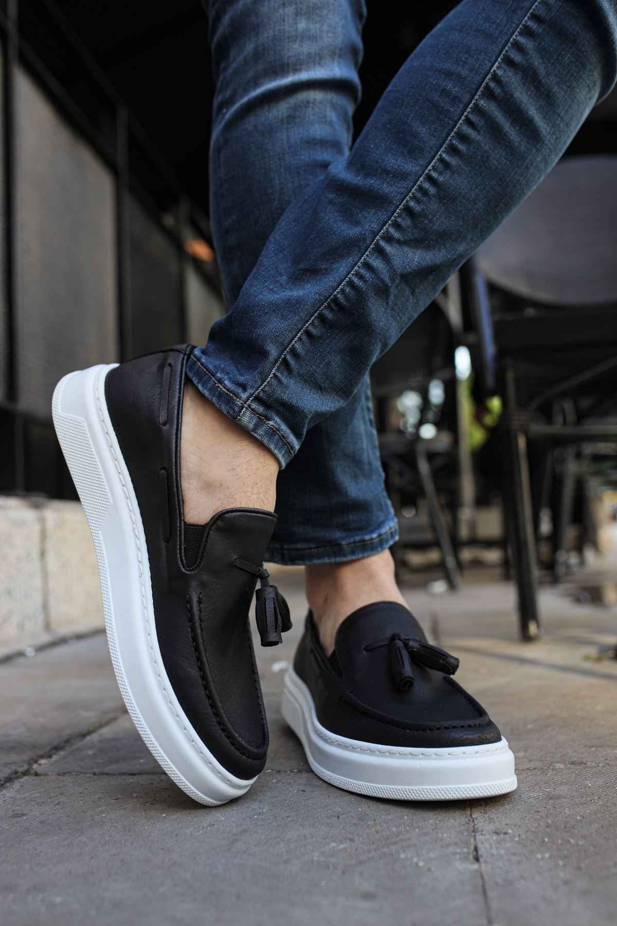 Men's black loafers with tassel strap and white midsole, worn with jeans
