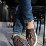 Brown loafers with tassel front and white sole, shown with jeans.