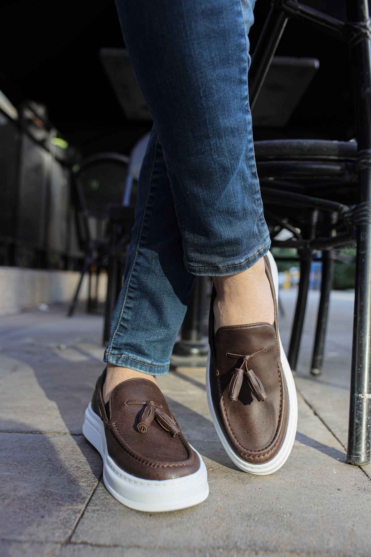 Brown loafers with tassel front and white sole, shown with jeans.