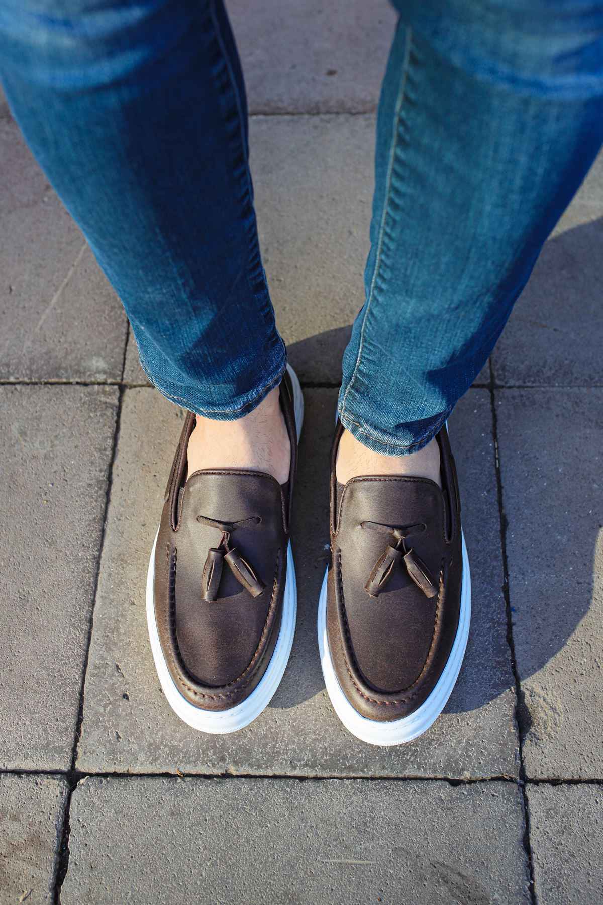 Brown loafers with tassel fronts and white soles, viewed from front.