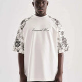 White oversized T-shirt with black floral print sleeves and small chest cursive