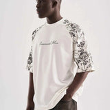 White oversized T-shirt with black floral sleeve print and draped front hem