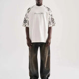 White oversized T-shirt with black floral print sleeves and center chest cursive text