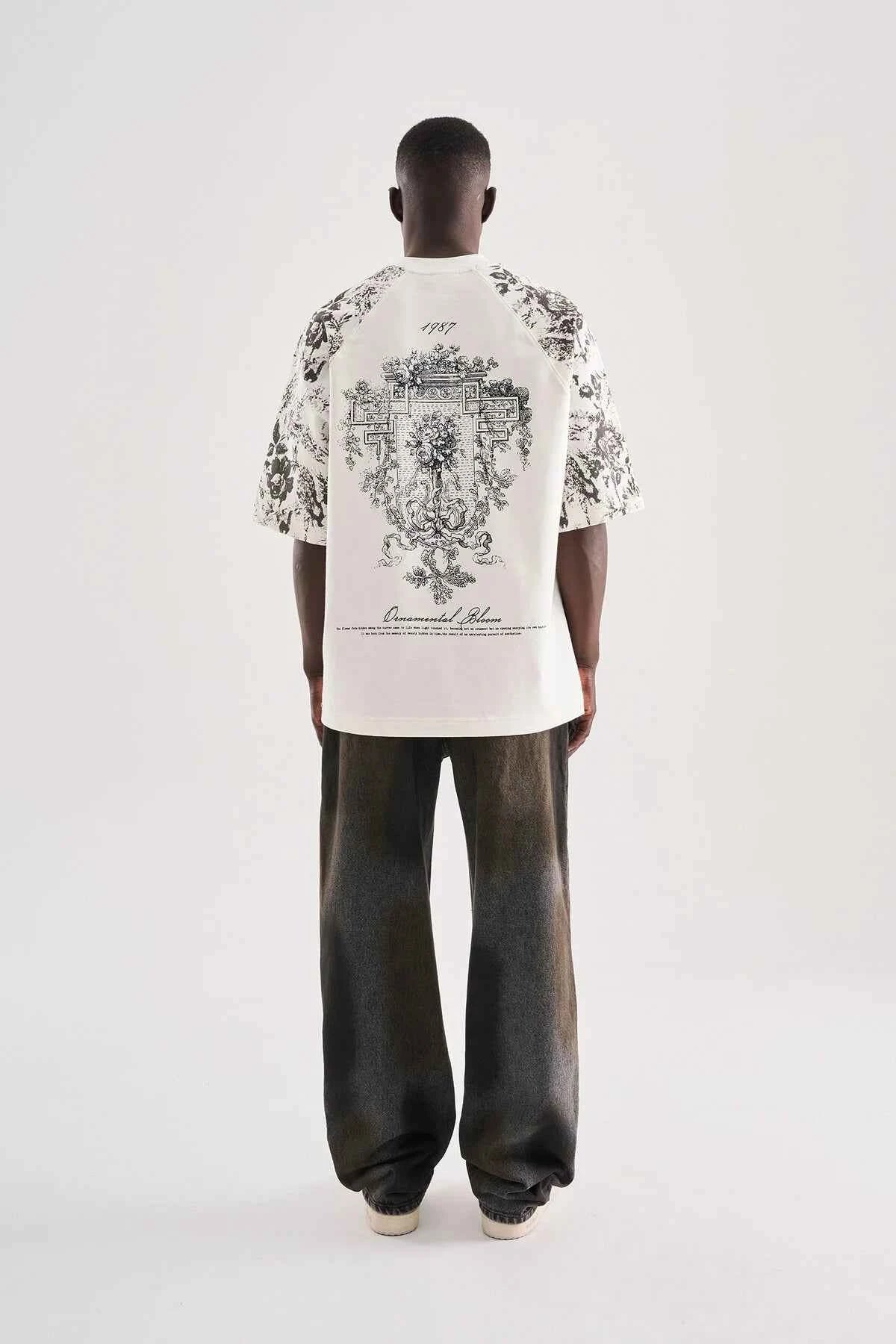 White oversized T-shirt with large black floral crest graphic on back, rear view