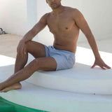 Mayom men's gray swimming shorts, seated on lounge edge