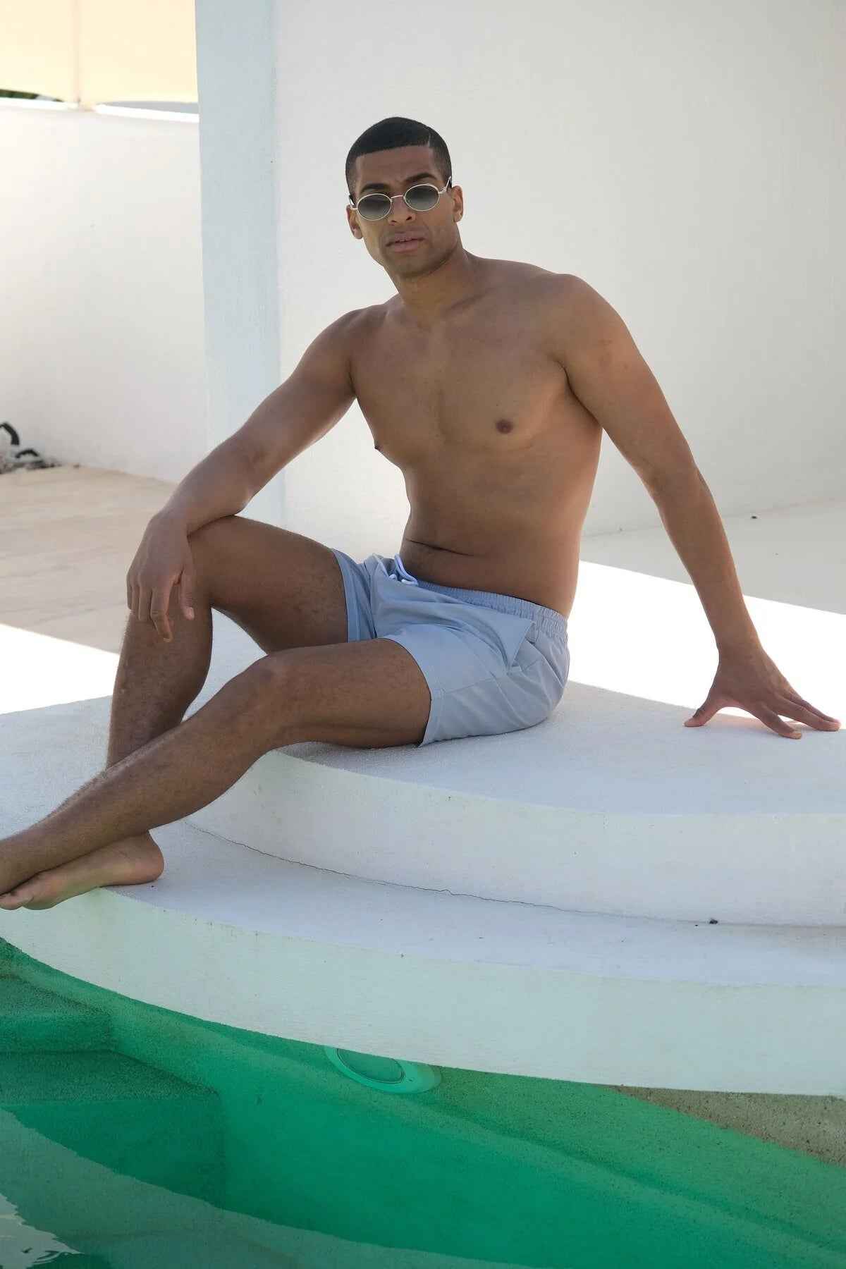 Mayom men's gray swimming shorts, seated on lounge edge