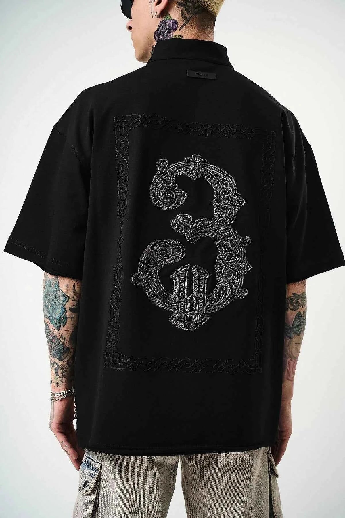 Men's black oversize half-zip T-shirt with large embroidered back graphic detail.