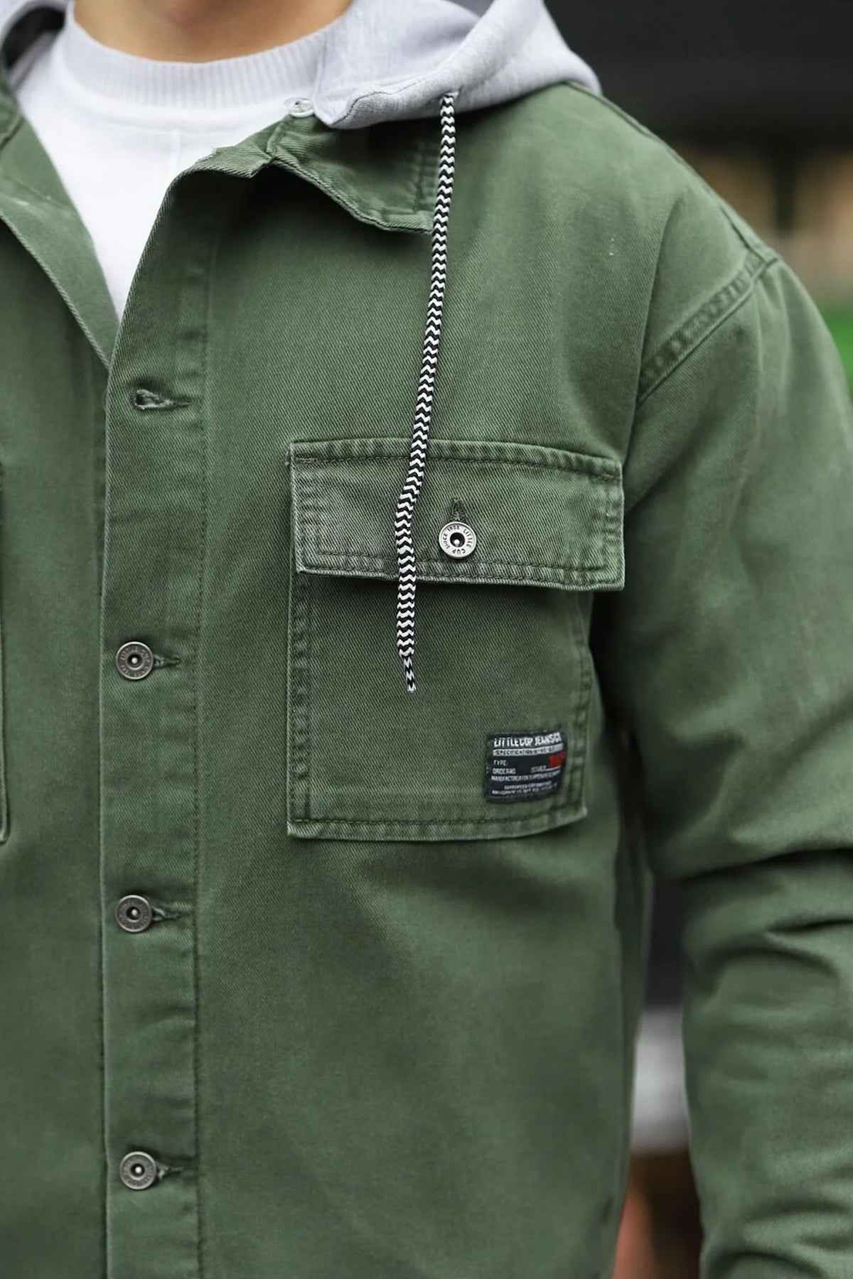 Olive denim jacket chest pocket with flap, button, and hanging chain detail