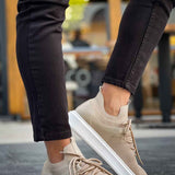 Beige knit sneakers with lace-up front and white rubber sole, worn with dark pants