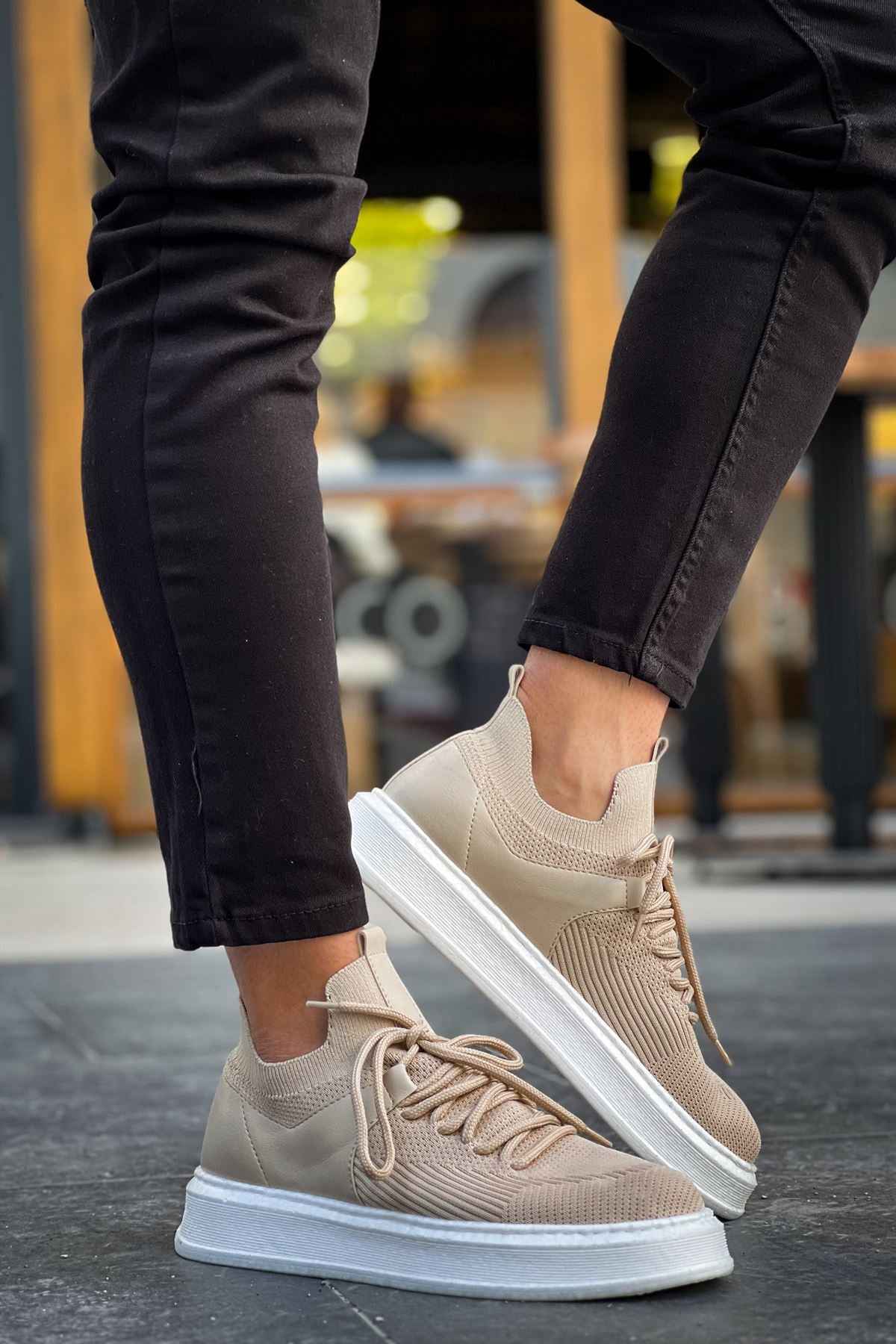 Beige knit sneakers with lace-up front and white rubber sole, worn with dark pants
