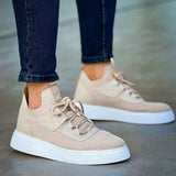 Beige knit sneakers with lace-up front and white rubber sole, worn with dark jeans.