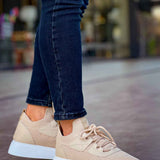 Beige knit lace-up sneakers with white sole, side view on dark jeans.