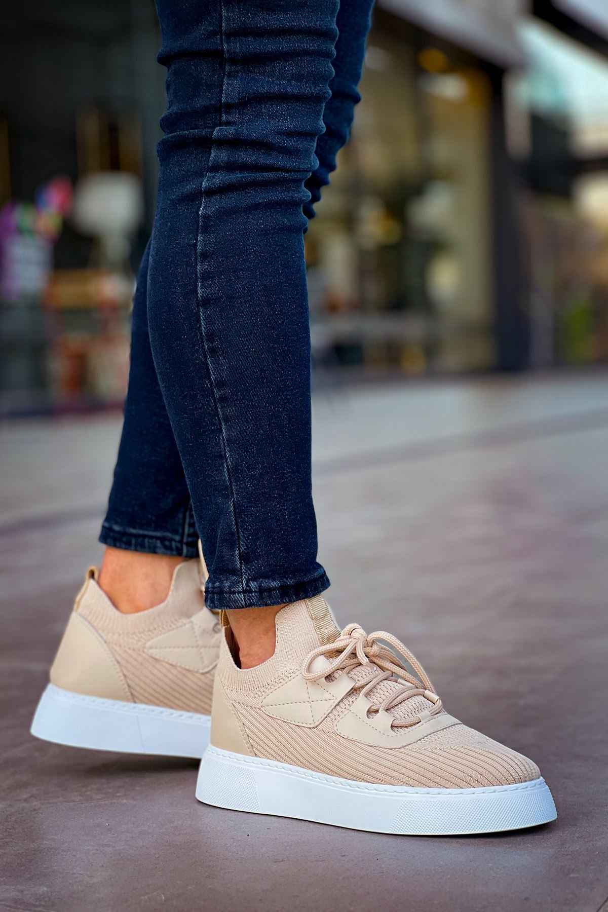 Beige knit lace-up sneakers with white sole, side view on dark jeans.