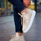 Beige knit lace-up sneakers with white sole and thick profile, shown with jeans.