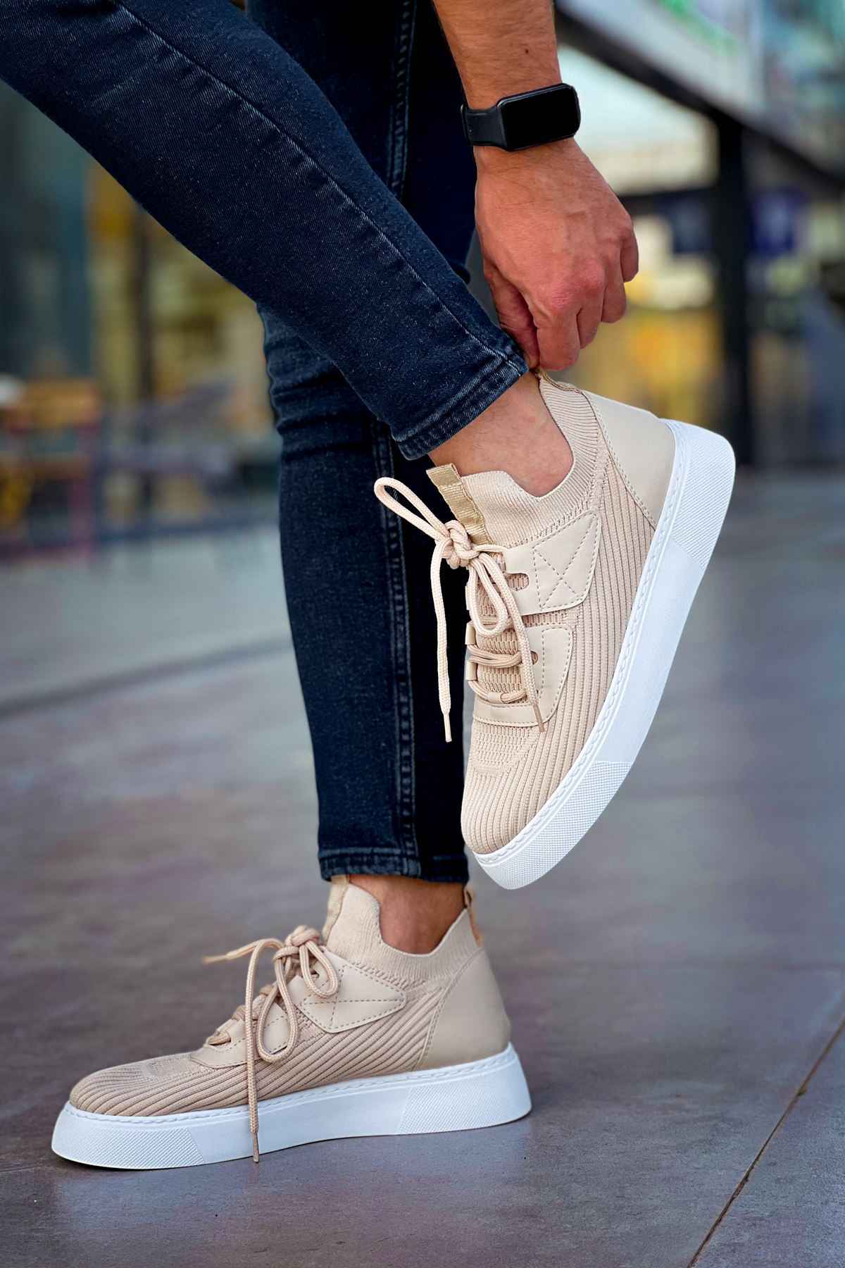 Beige knit lace-up sneakers with white sole and thick profile, shown with jeans.