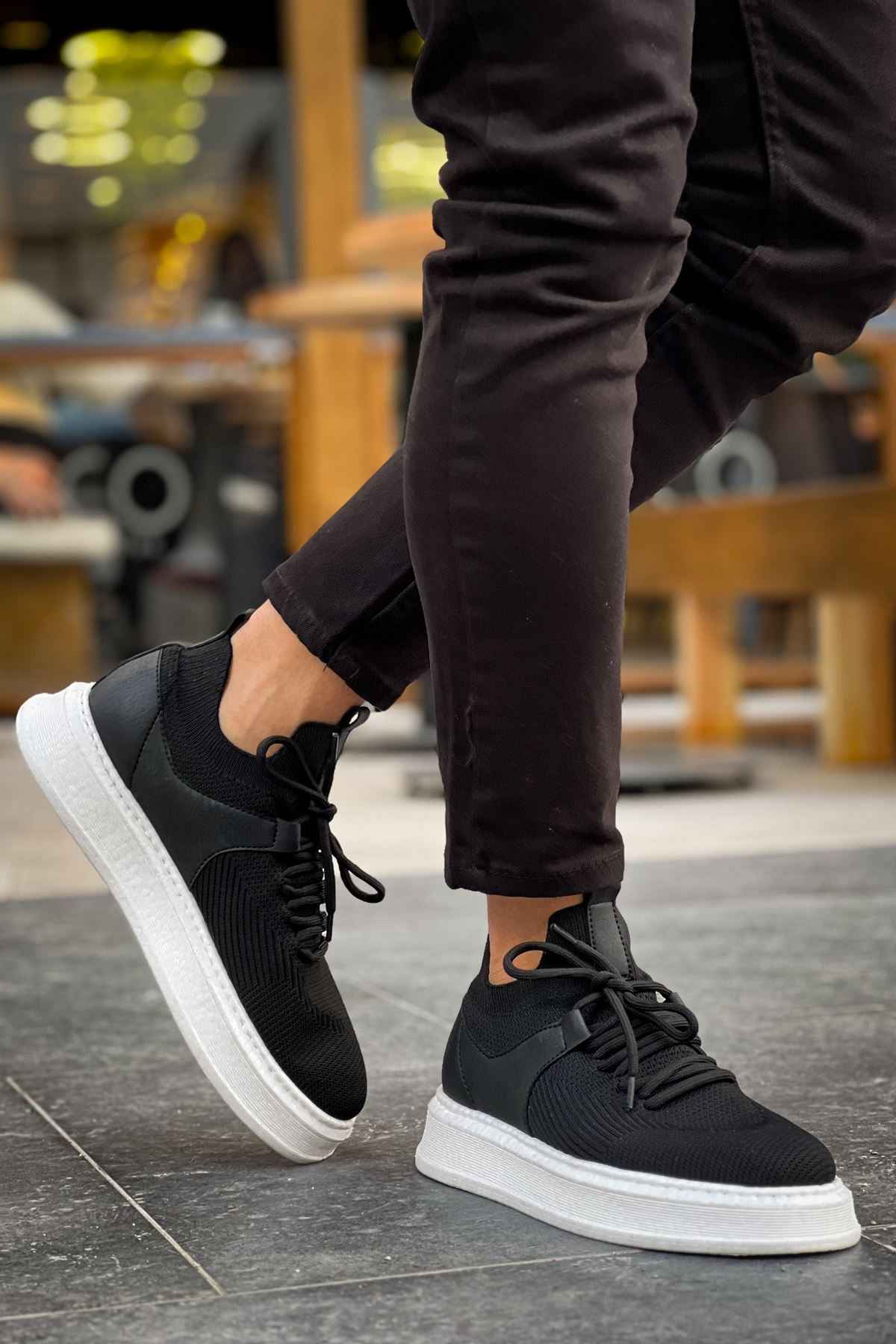 Black knit lace-up sneakers with white sole, stepping view.