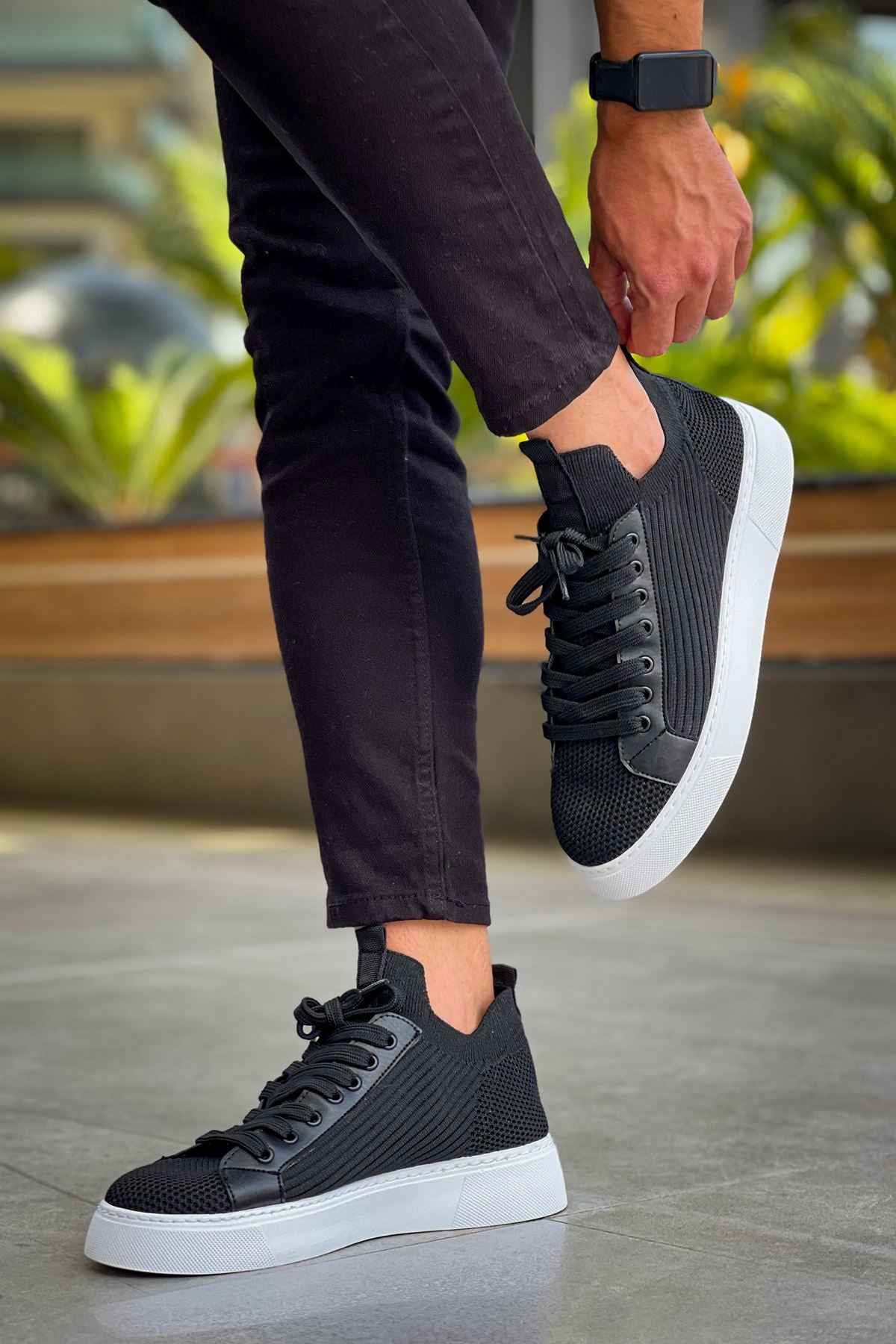 Men's black knit sneakers with lace-up front and white sole, walking pose