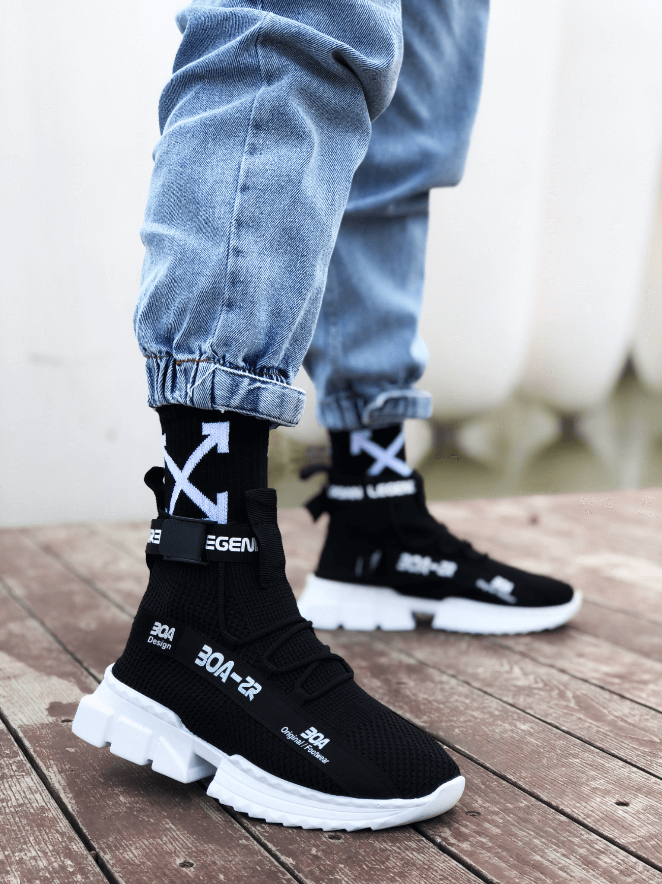 Black knit sneakers with white sole, hook-and-loop strap, and X-pattern detail