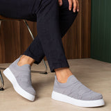 Gray knit sneakers with white sole, on feet seated, angled view