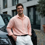 Mens pink dress shirt with button front, spread collar, long sleeves, worn untucked with white pants.