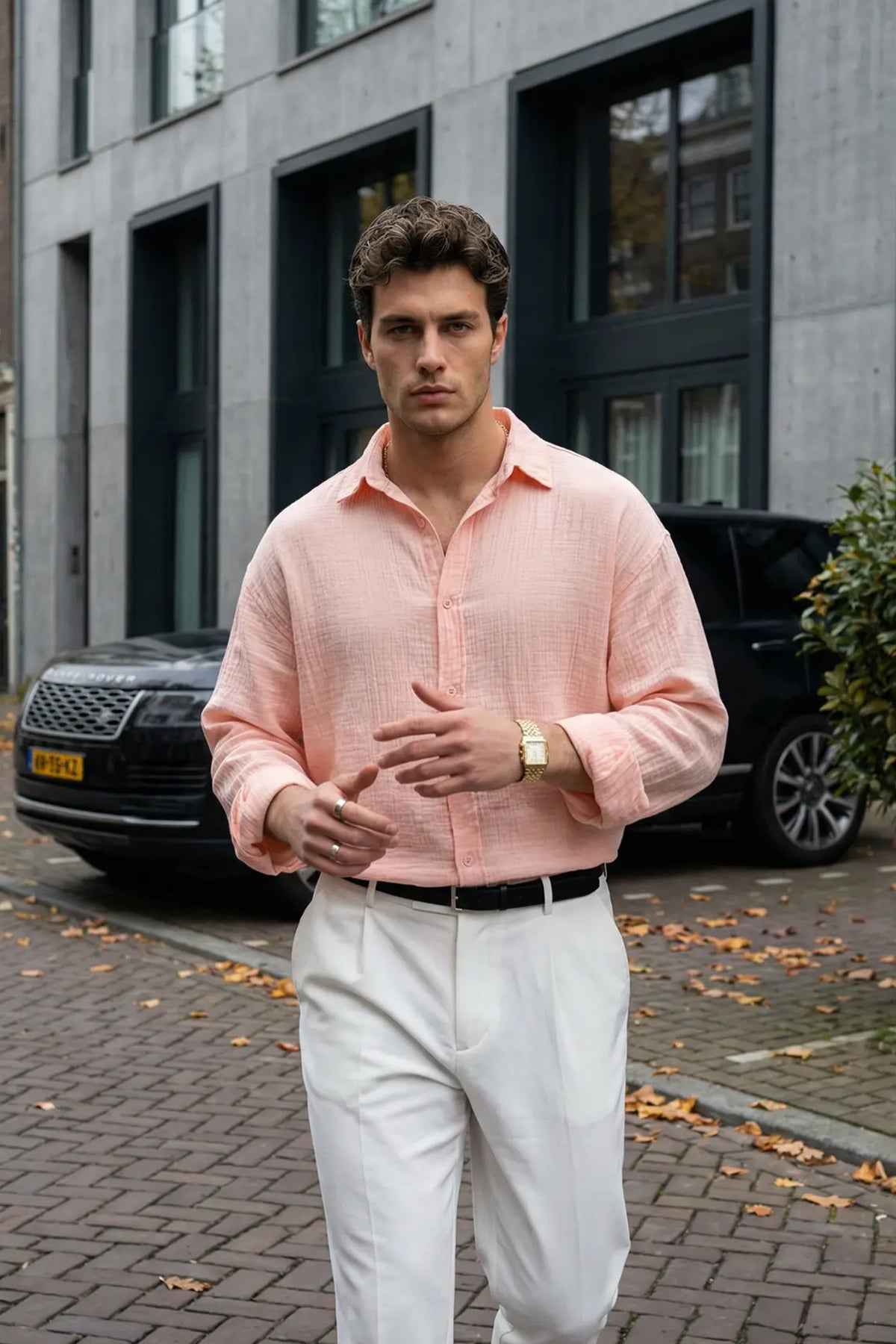 Mens pink button-up dress shirt with spread collar and long sleeves, paired with white trousers.