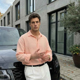 Mens pink dress shirt with button front and spread collar, long sleeves, styled with white pants.
