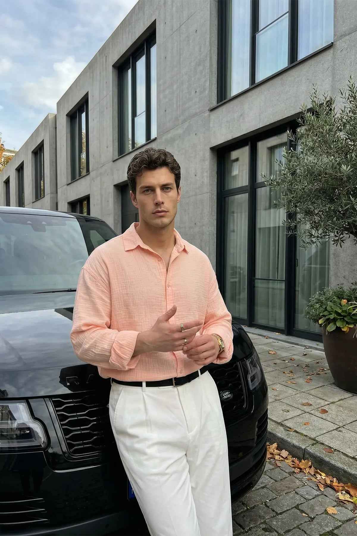 Mens pink dress shirt with button front and spread collar, long sleeves, styled with white pants.