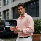 Mens pink button-up dress shirt with spread collar, long sleeves, tucked into white trousers.
