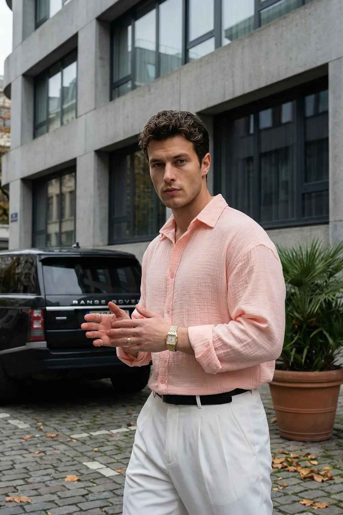 Mens pink button-up dress shirt with spread collar, long sleeves, tucked into white trousers.