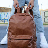 Tan leather backpack with front zipper pocket and top handle, held in hands