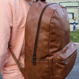 Tan leather backpack with front zip panel, side pocket tabs, and adjustable straps