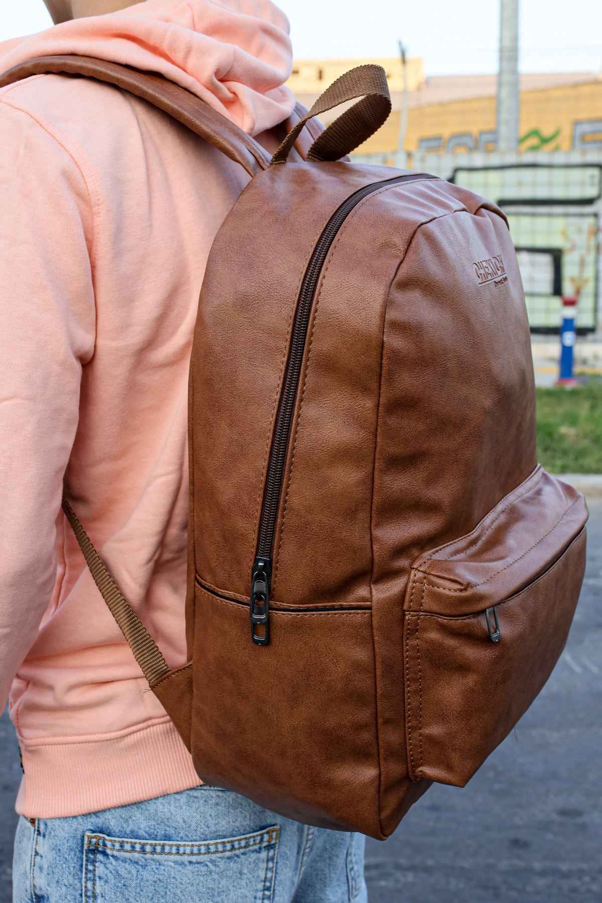 Tan leather backpack with front zip panel, side pocket tabs, and adjustable straps