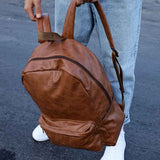 Tan leather backpack with curved front pocket, webbing straps, and top carry handle