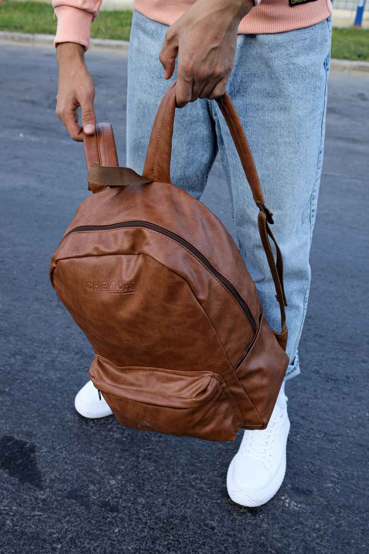 Tan leather backpack with curved front pocket, webbing straps, and top carry handle