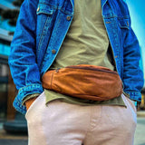 Tan leather crossbody bag worn across chest, zipped front and adjustable strap