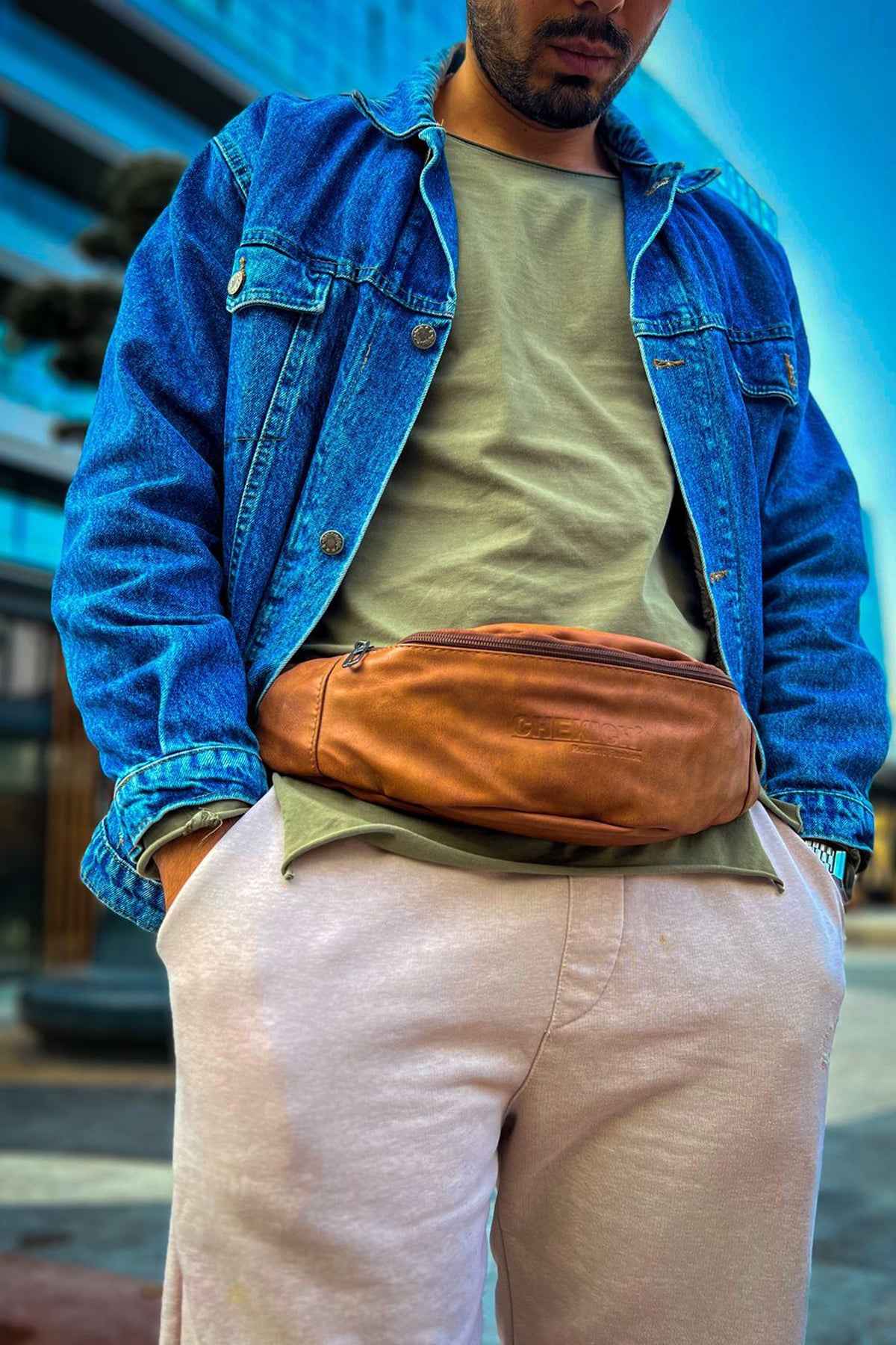 Tan leather crossbody bag worn across chest, zipped front and adjustable strap