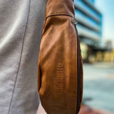 Tan leather crossbody bag with zipper and textured finish, side view with logo