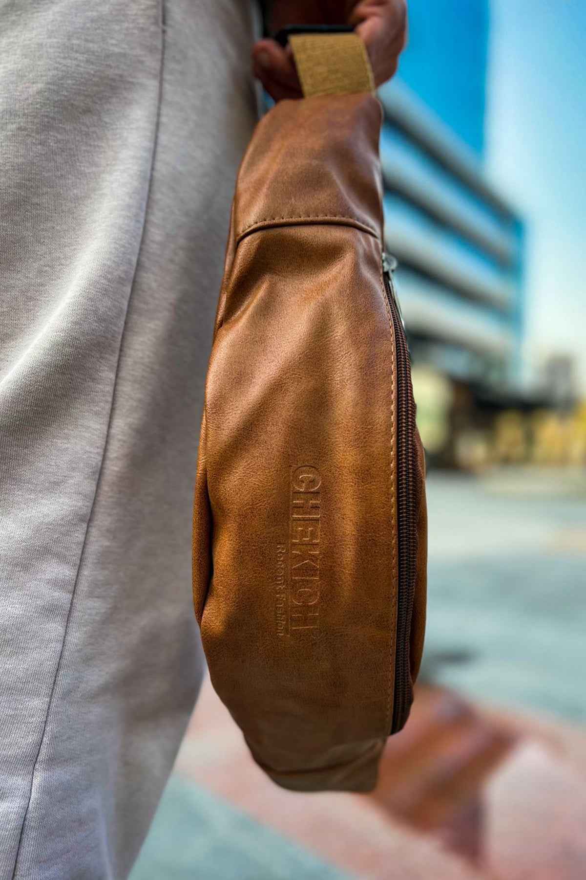 Tan leather crossbody bag with zipper and textured finish, side view with logo