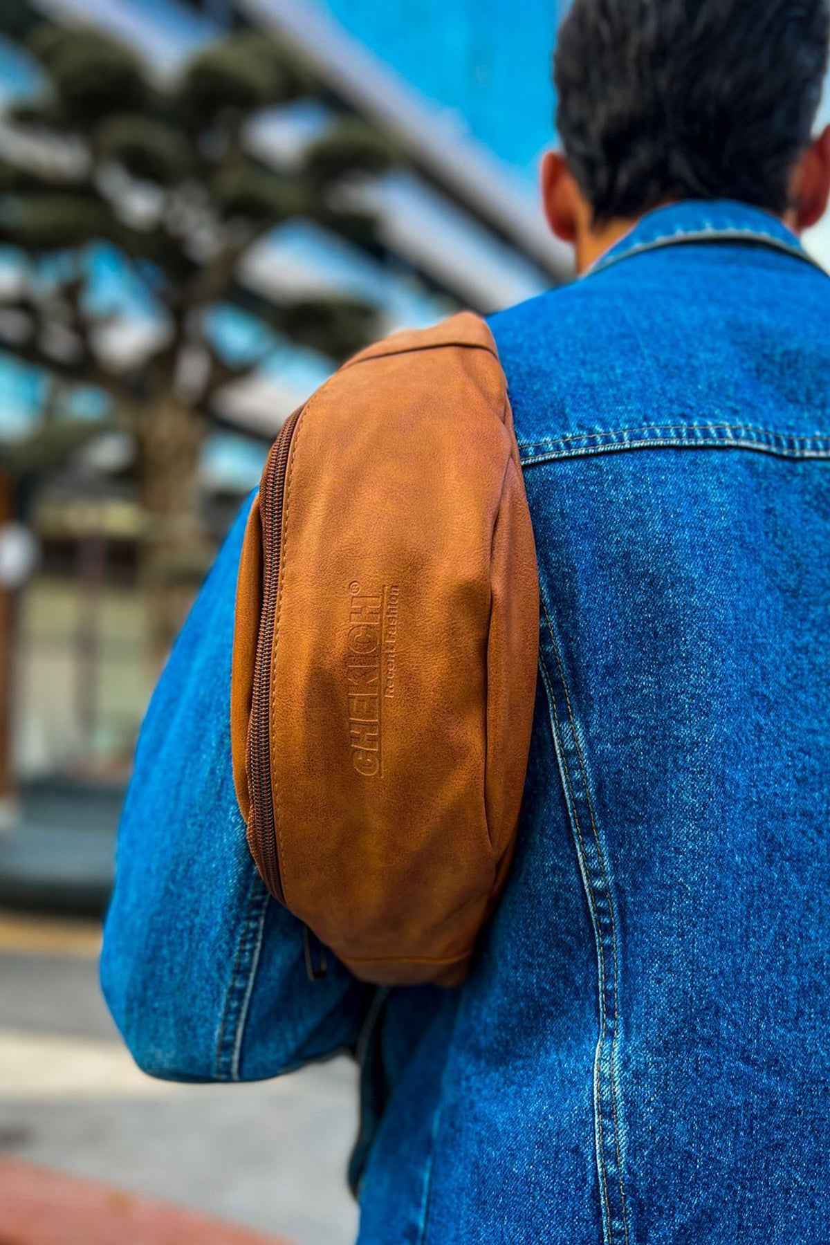 Tan leather crossbody bag side/back view with zip pocket on denim jacket