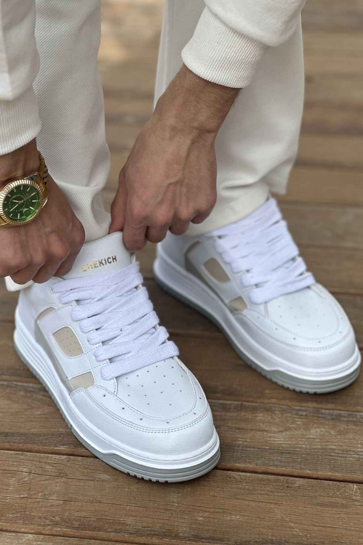 White and beige lace-up sneakers, pair worn with white pants, close front view