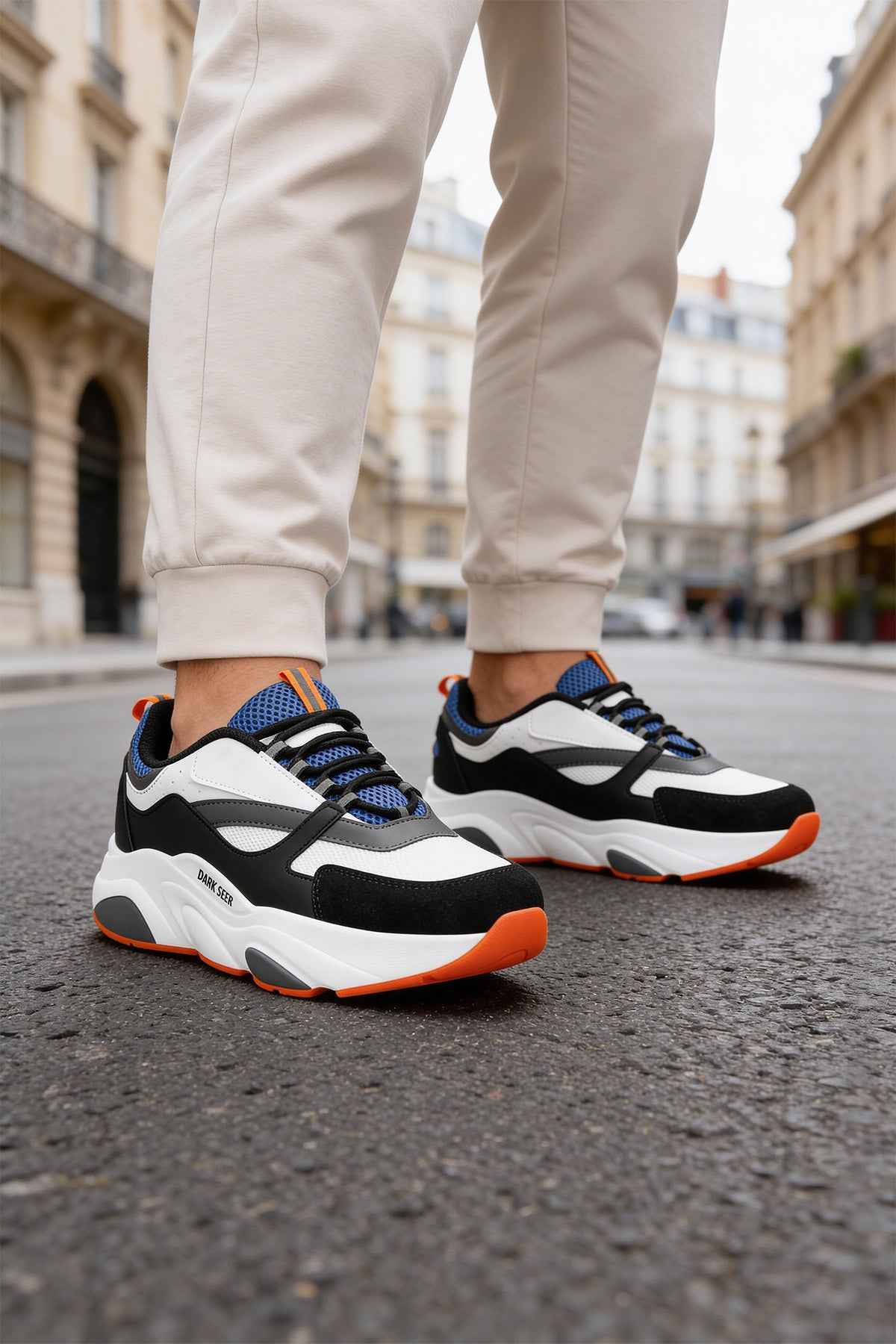 Men's lace-up sneakers, side view: white and black uppers with blue panels; orange soles.