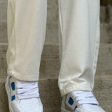 Men's white sneakers with blue panels and cushioned sole under cream pants