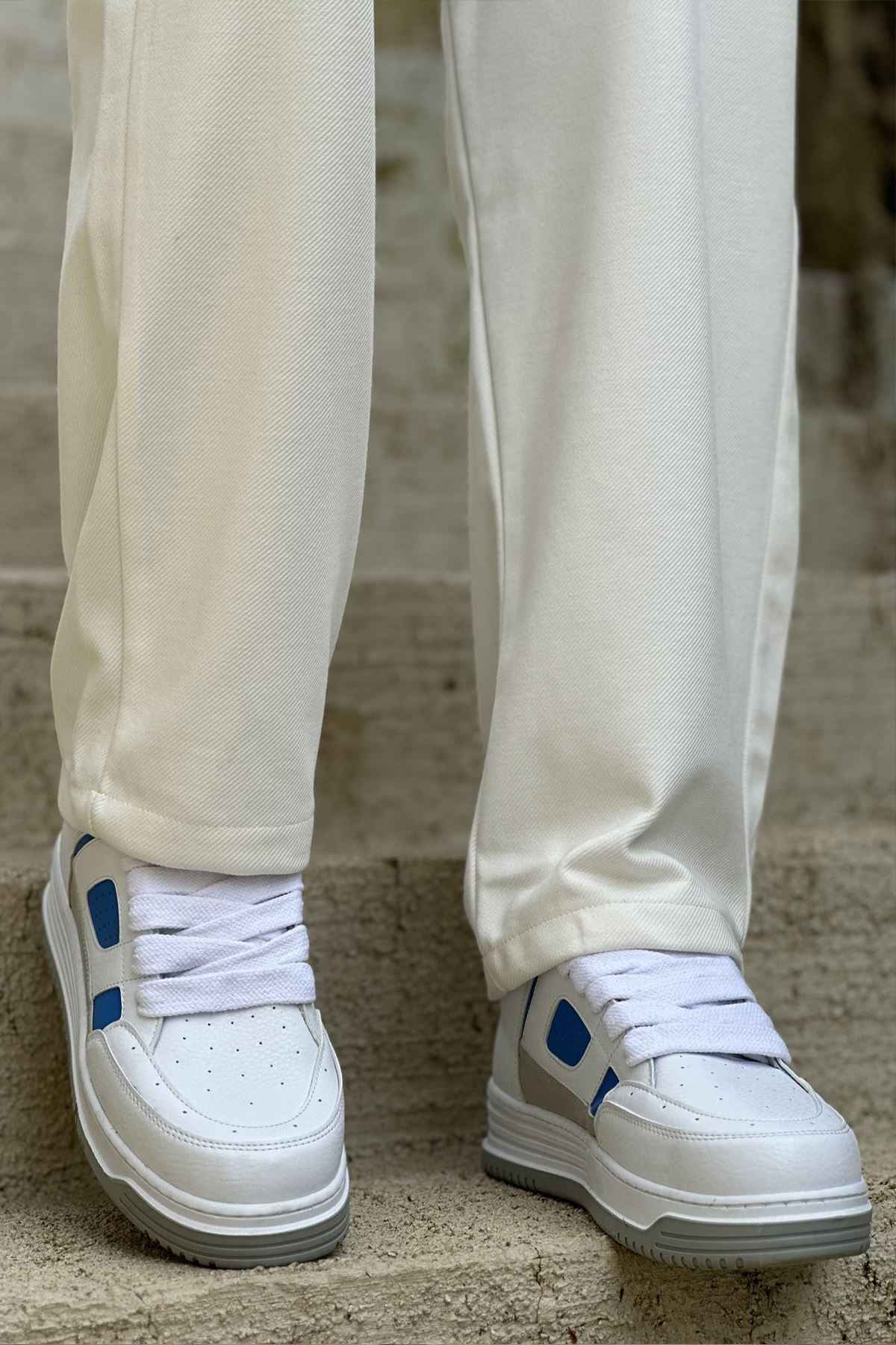 Men's white sneakers with blue panels and cushioned sole under cream pants