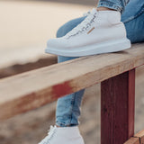 White lace-up boots shown on a wooden railing with denim cuffs